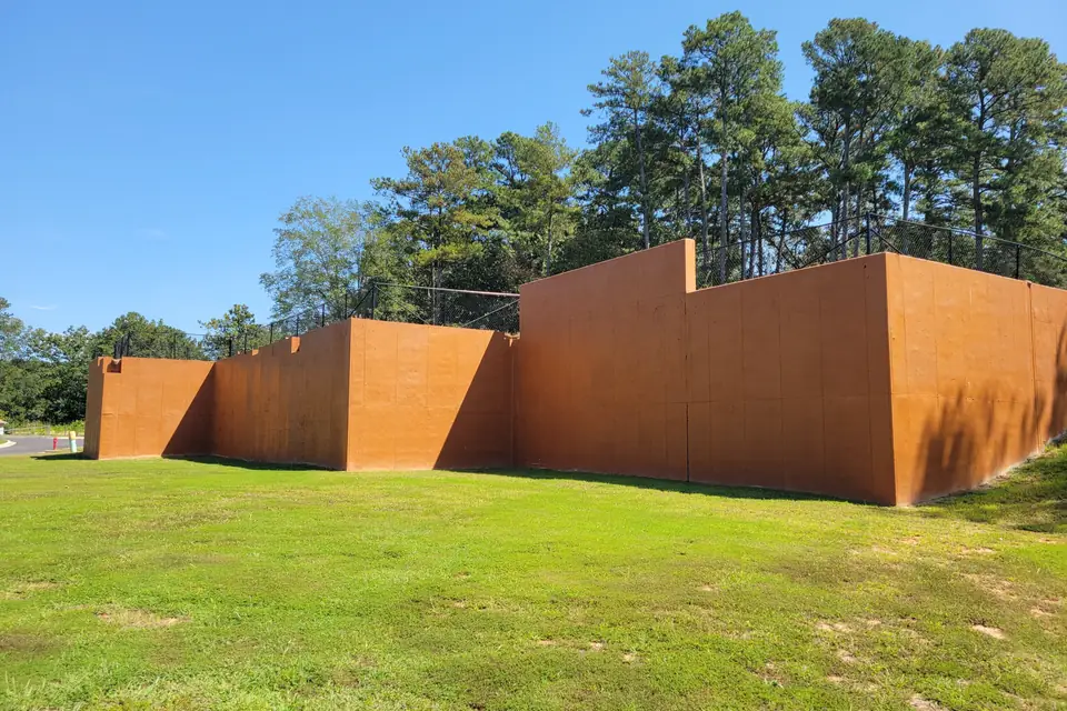 Two tall poured concrete retaining walls with a rust-colored face holding back a wooded hillside
