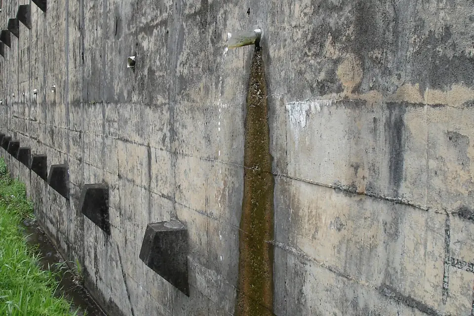 Water draining from a pipe outlet in the face of a concrete retaining wall