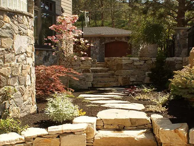 Stone retaining walls and steps forming planting beds beside a house