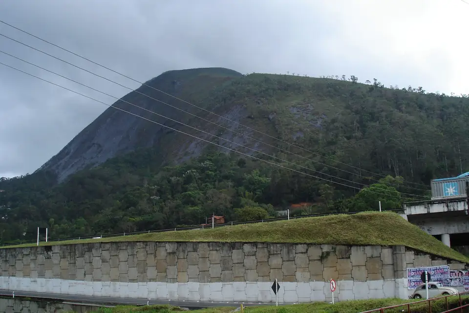 A concrete block gravity retaining wall holding a grassy embankment along a road