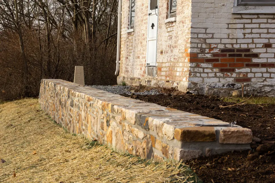A newly built low stone retaining wall along a freshly graded front yard beside a brick house