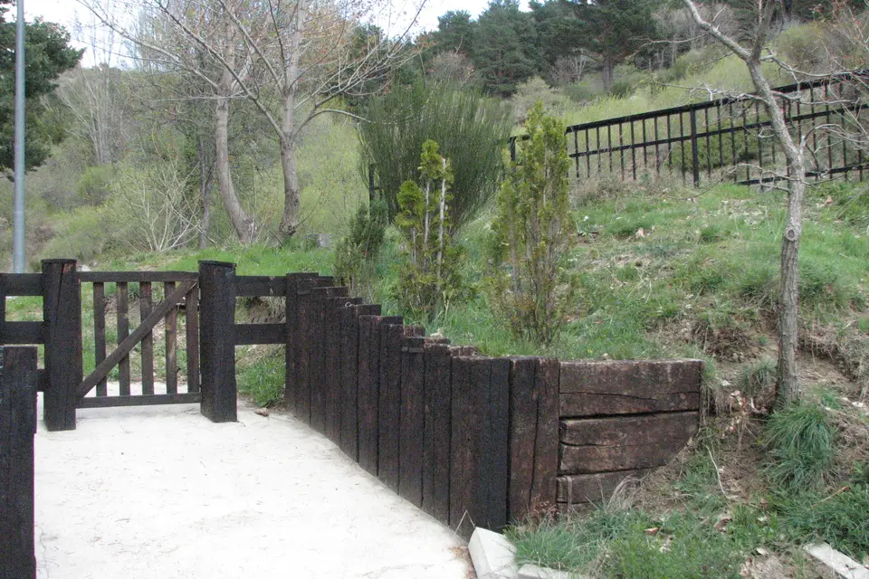 A timber retaining wall built from dark railroad ties beside a garden path and wooden gate
