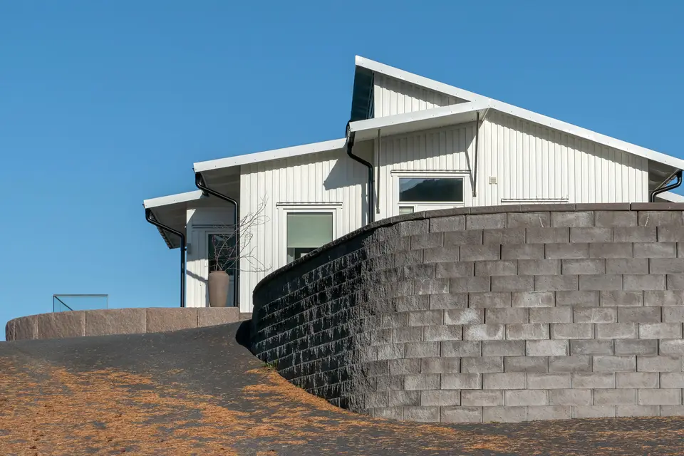 A tall curved segmental block retaining wall holding the hillside below a modern white house